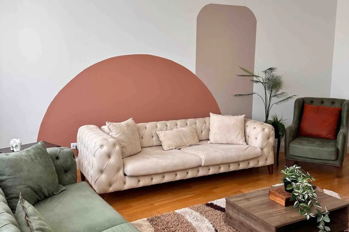 Living room with multiple comfy pink and green couches. Plants and cool wall art.