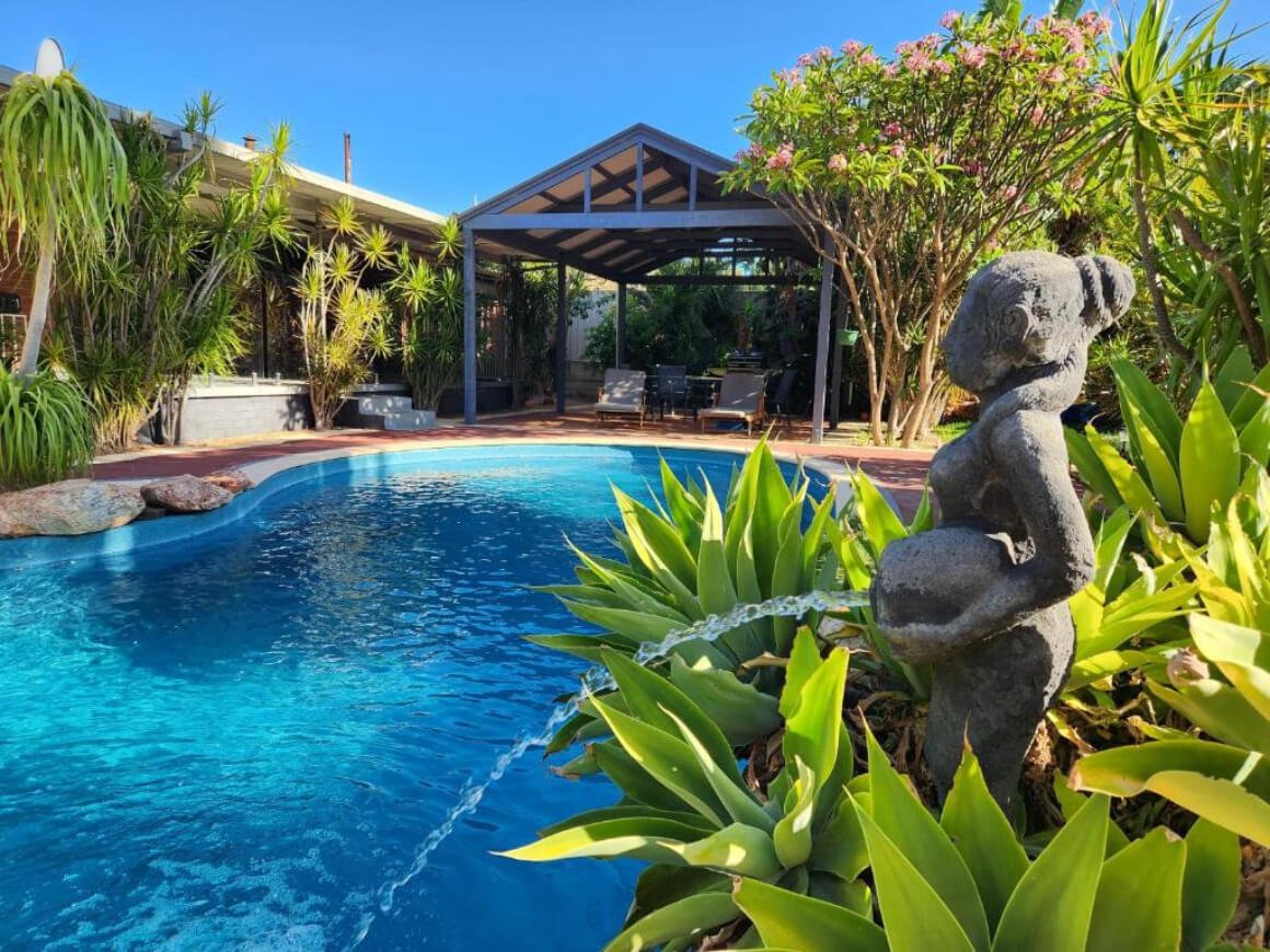 View of pool and pool house with loungers. Water fountain statute in the foreground.