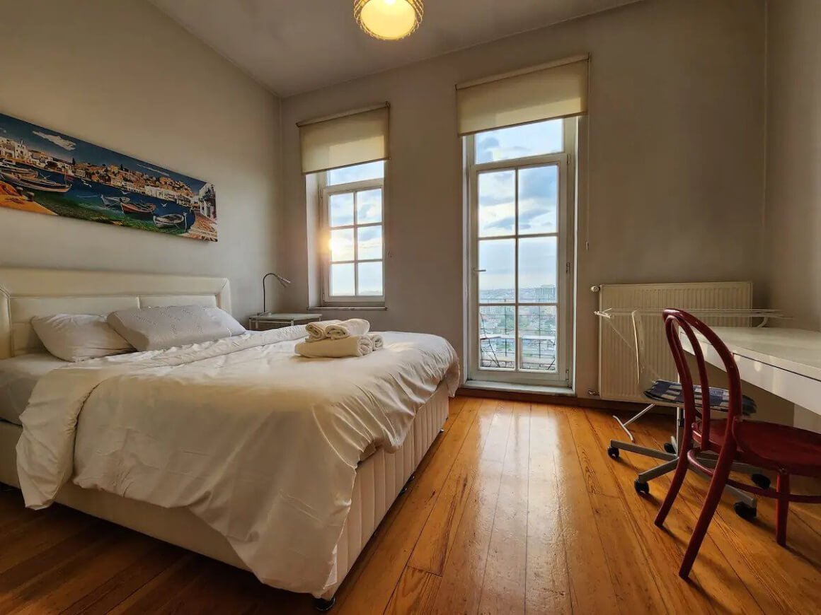Comfy room with large bed, desk, chair and large window with door out to a small terrace
