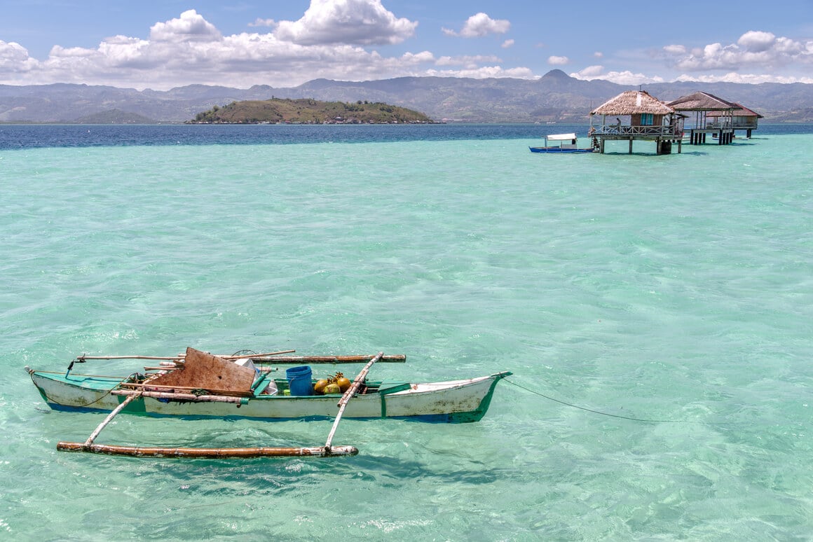 boat floating with overwater bangallows and a mountain in the background 