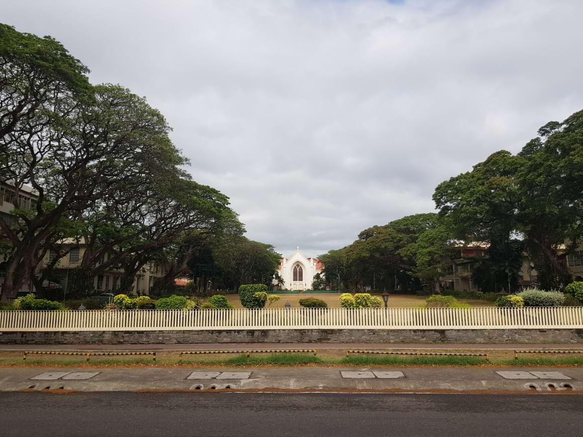 white building in a large green field surrounded by trees in Silliman Dumaguete