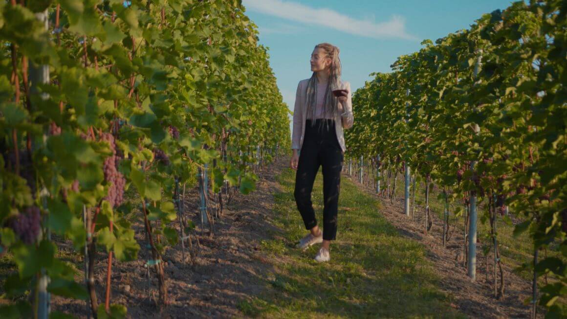 a woman wallking through a lane of a georgia vineyard while holding a glass of wine
