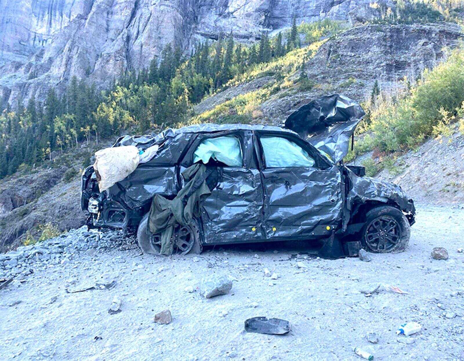 a smashed up green car on the side of a dirt road in pakistan