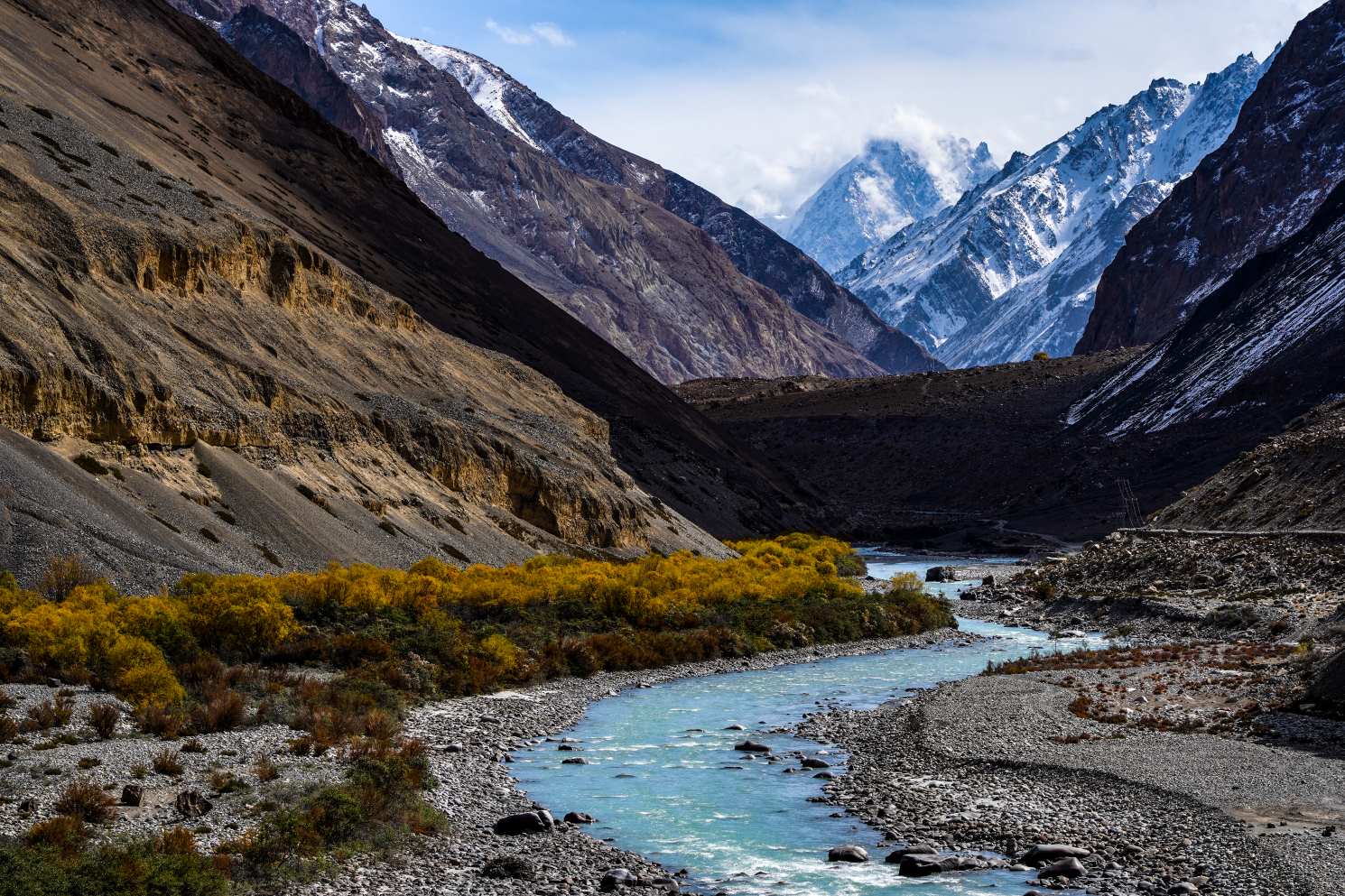 bright blue river flanked by yellow shrubs and snowcapped mountains in the background in hunza valley gilgit baltistan pakistan