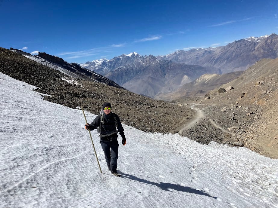 man trekking up a snowy incline in nepal's annapurna regio while holding a wooden stick