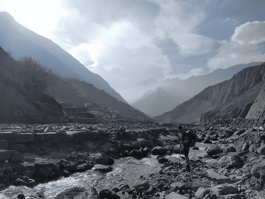 man with a trekking pole about to cross a river while trekking in nepal