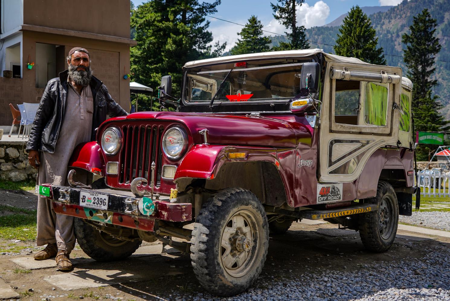 man standing with an old maroon colored jeep in a remote area of northern pakistan