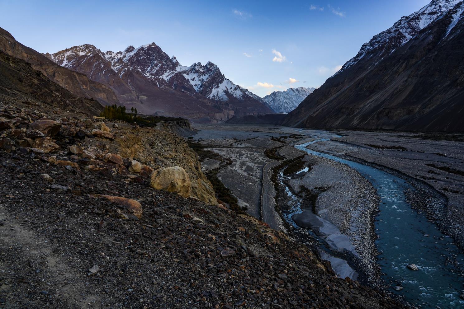 a view of purplish red mountains and a blue river at sunset while driving in shimshal valley in pakistan
