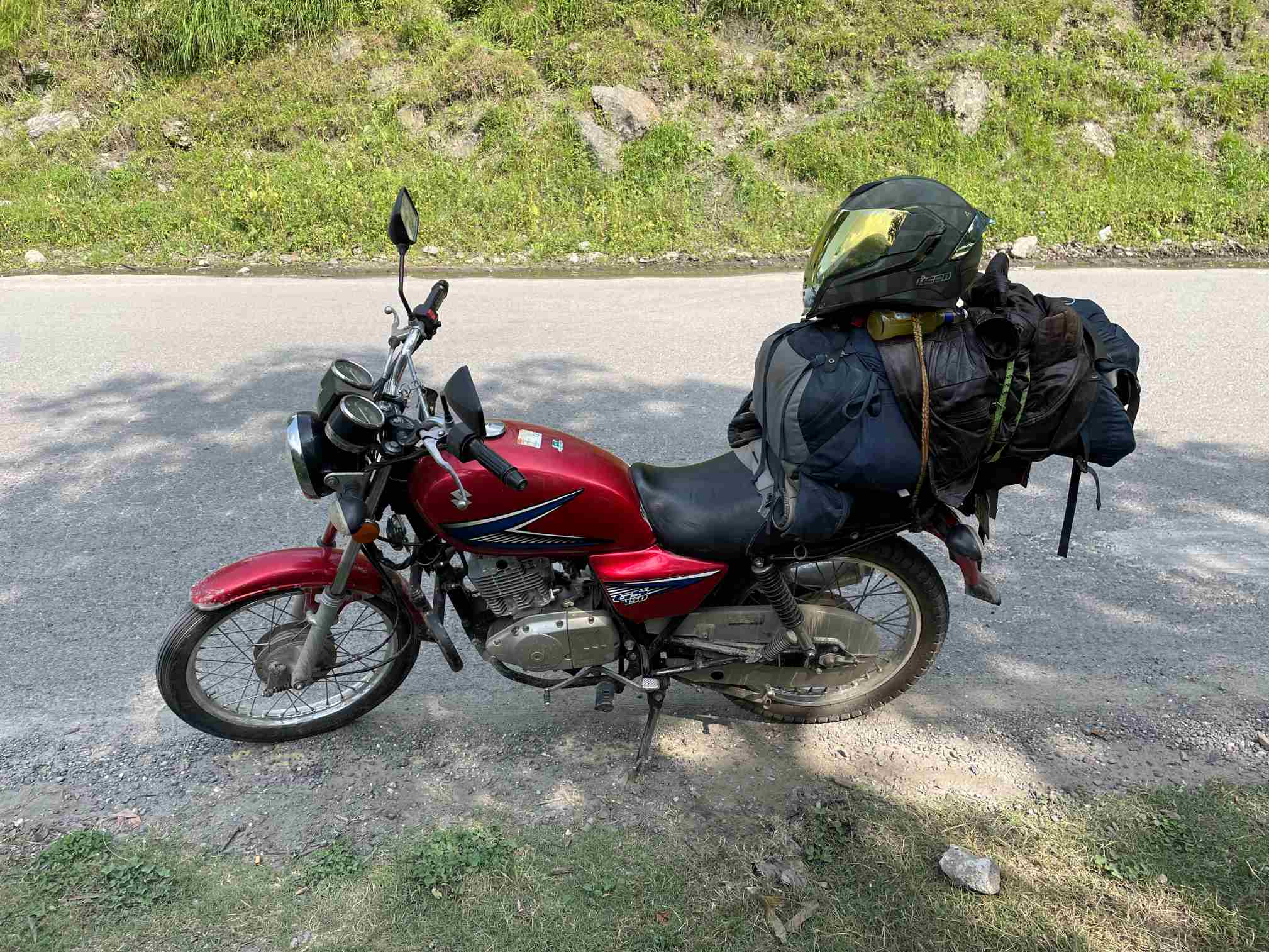 red motorcycle parked on a paved street overloaded withg a huge backpacking backpack in pakistan