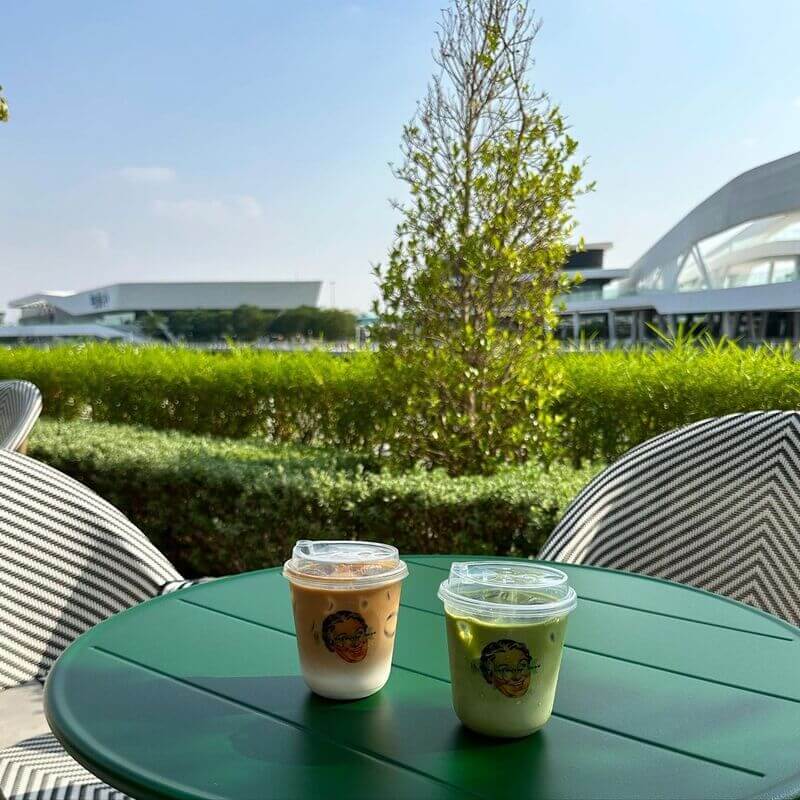 A cup of coffee and matcha on coffee shop table with a lush garden in the background