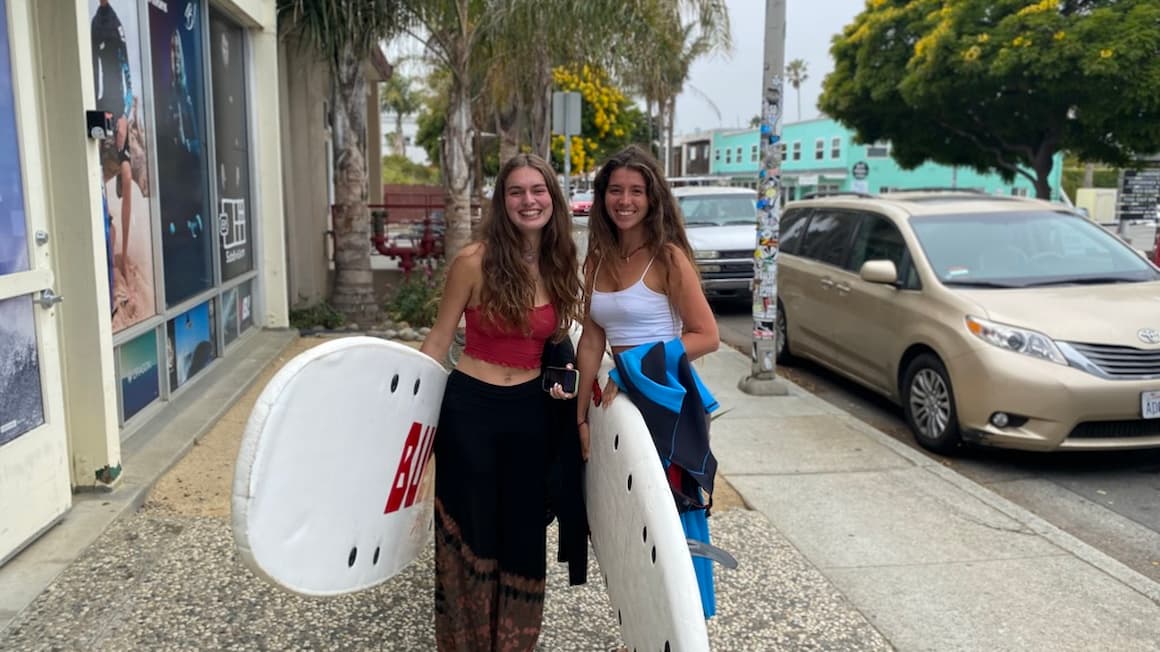 2 girls holding surfboards headed to the beach