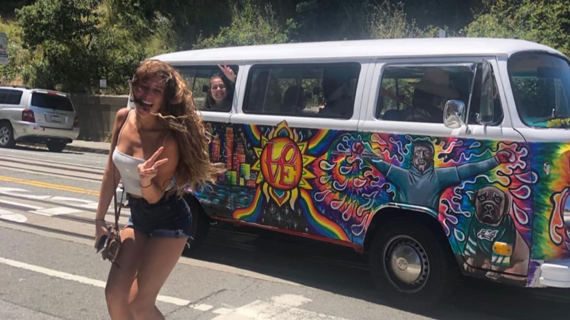 A girl smiling in front of a hippie van in California