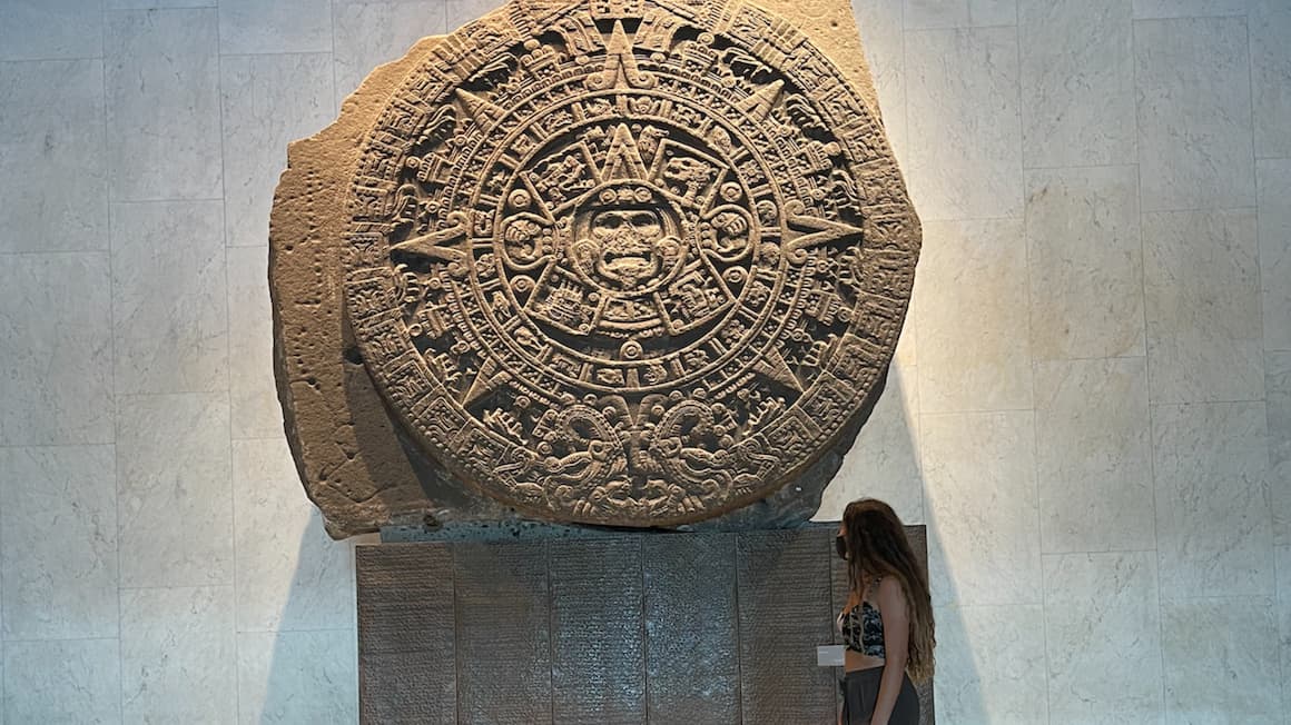 a girl standing in front of a rock artifact at an archeology museum