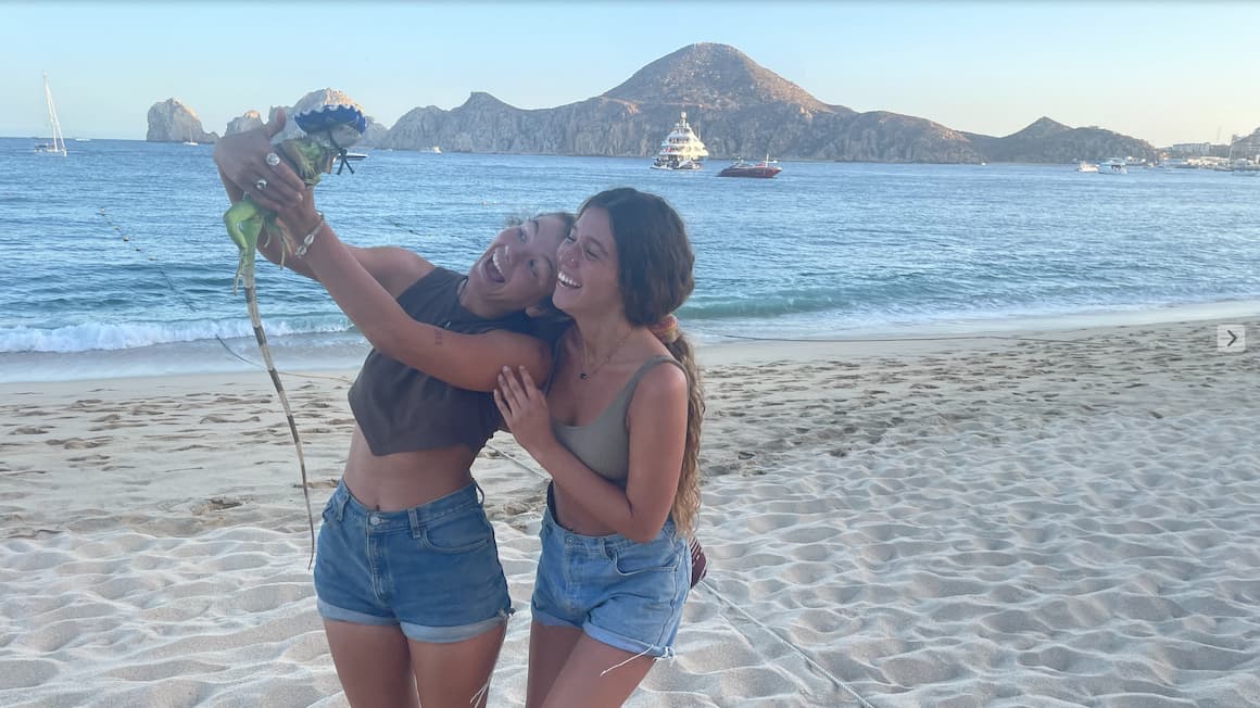 two friends on a beach in mexico holding a lizard that has a Sombrero on