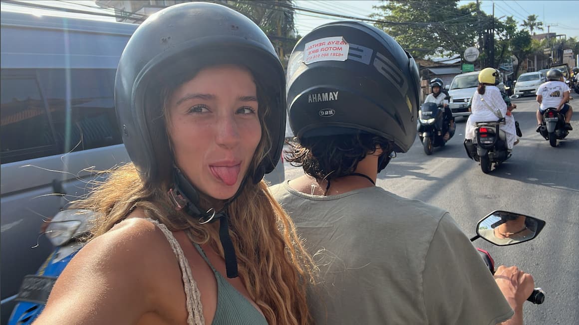 a girl taking a selfie wearing a helmet as she rides on the back of a scooter.