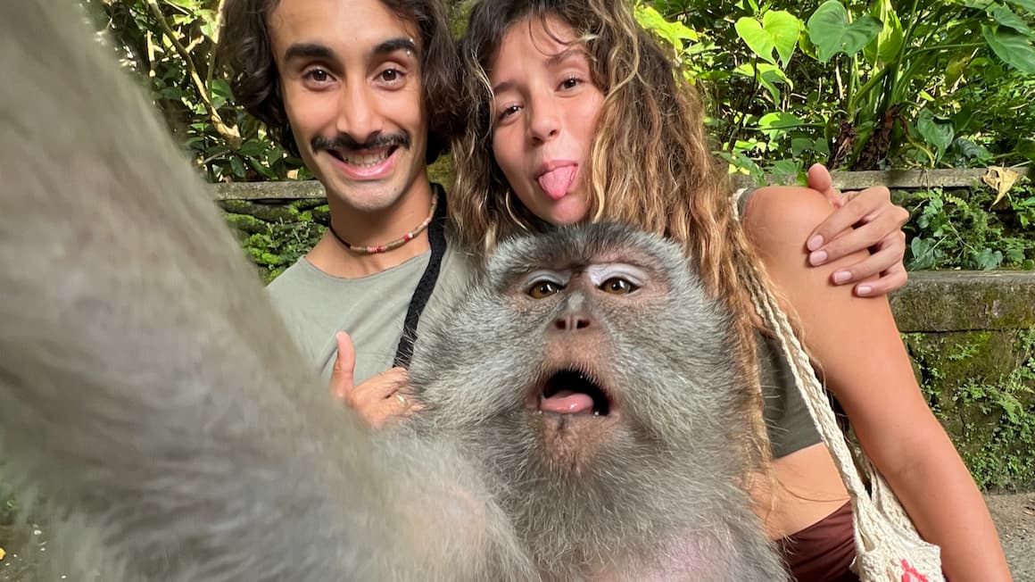 a couple taking a selfie with a monkey in the monkey forest of ubud, bali 