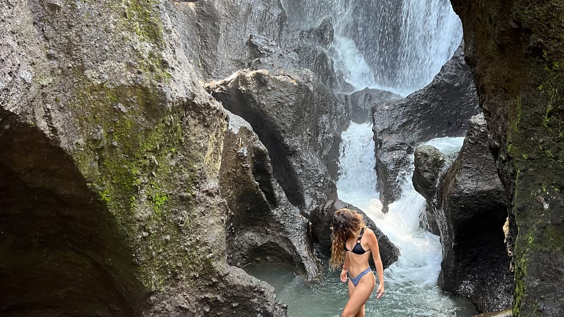 a girl walking on a log in front of pejeng kelod waterfall in bali indonesia 