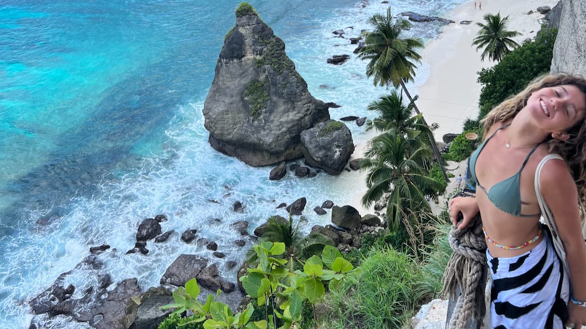 a girl smiling walking down a paved path down a cliff to a beach in nusa penida 