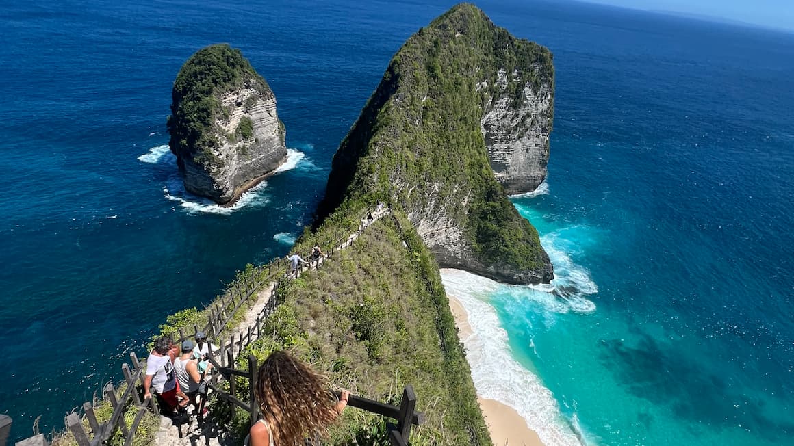 a girl climbing down to a famous beach with cliffs and clear blue ocean in nusa penida