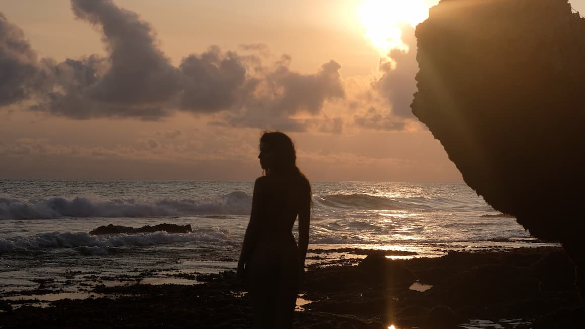 a girl at the beach as the sun sets on the ocean 