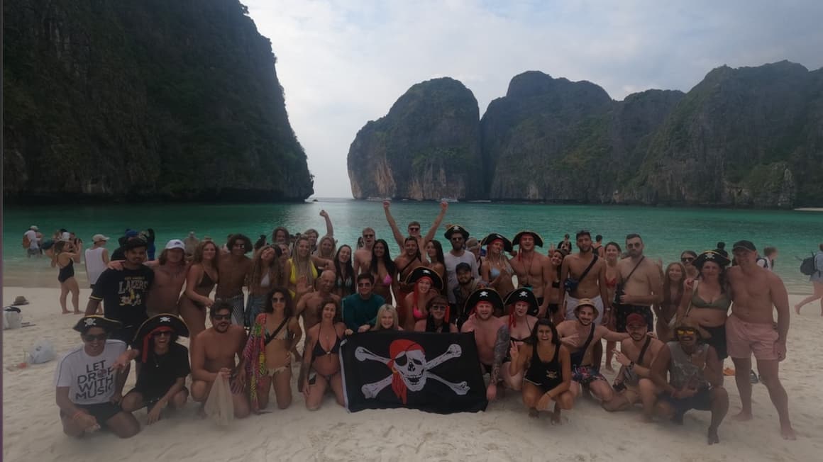 a big group of people at maya beach in thailand, gathering for a group picture acting like pirates
