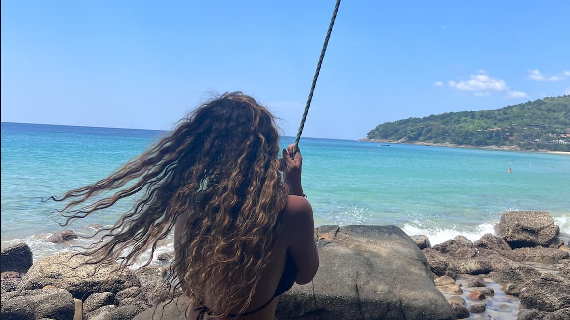 a girl swinging on a rope swing on a calm beach in phuket, thailand