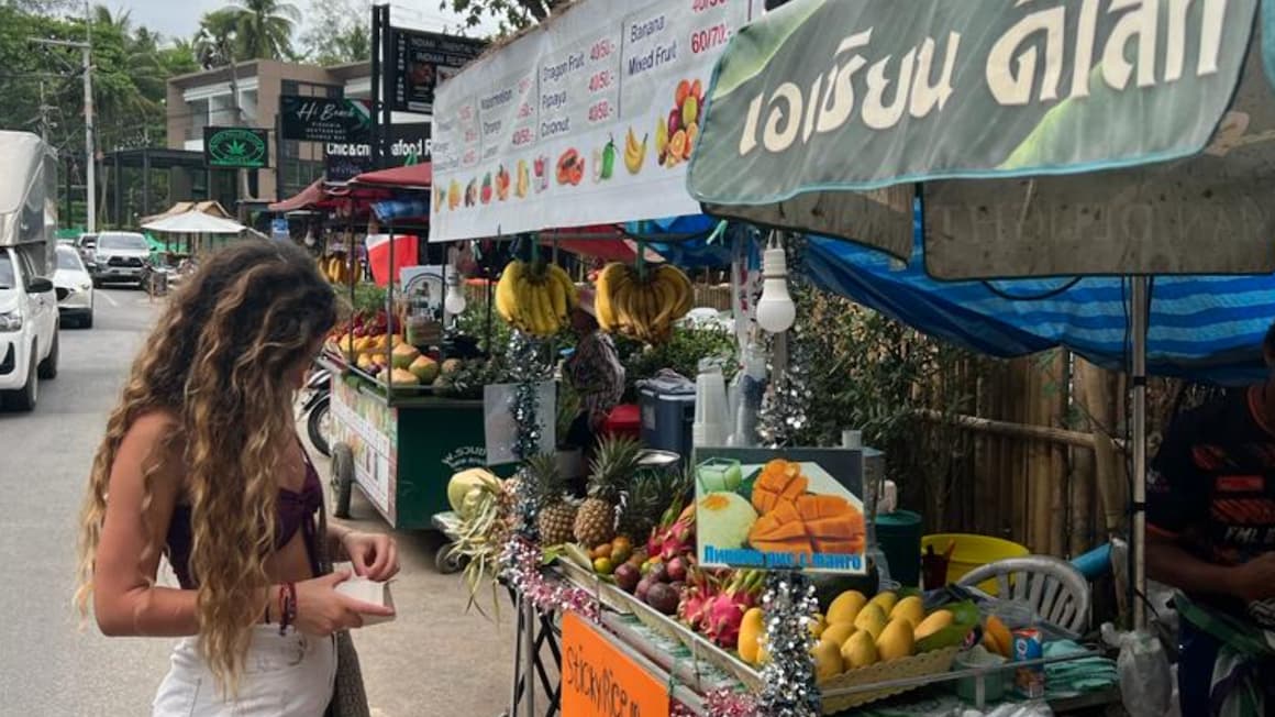 a girl buying fruit from a local fruit stand in phuket, thailand