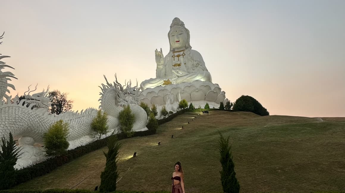 a girl standing in front of a buddhist statue in thailand 