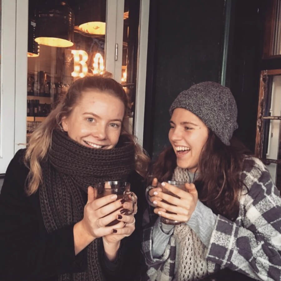 Two girls rugged up warm in scarfs and a beanie drinking mulled wine in a bar
