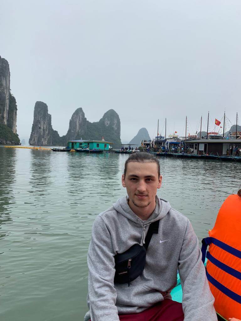Man on a boat ride in Ha Long Bay, Vietnam with a harbor and rock formations in the backdrop