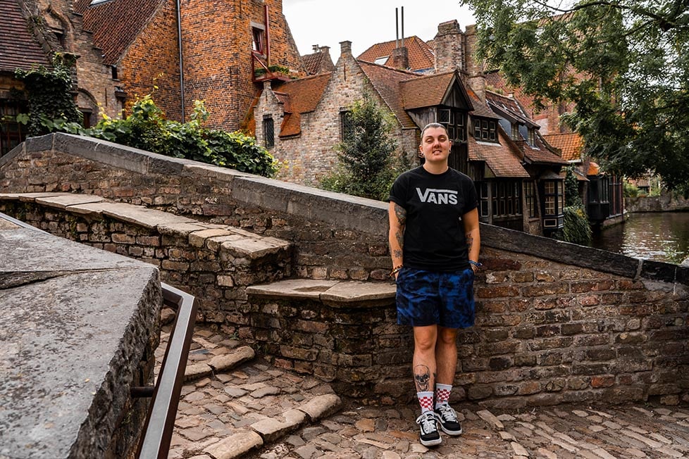 A smiling person on an old street with Bruges' canal in the background.