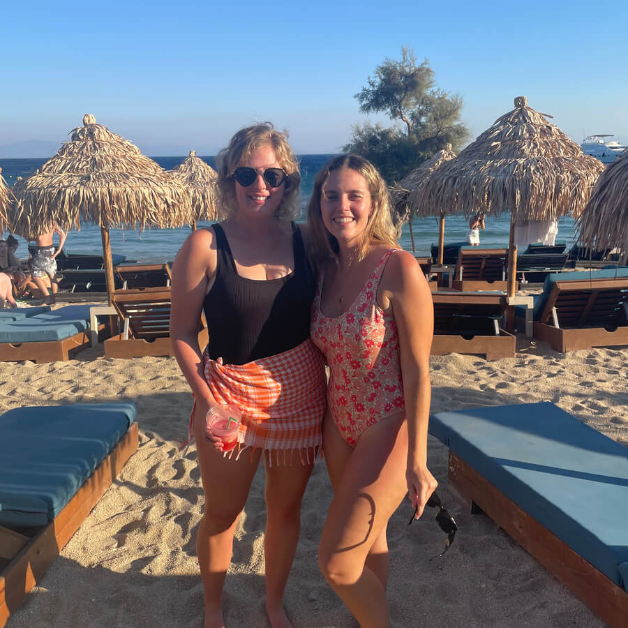 Two girls at the beach on a sunny day surrounded by sun beds and beach umbrellas