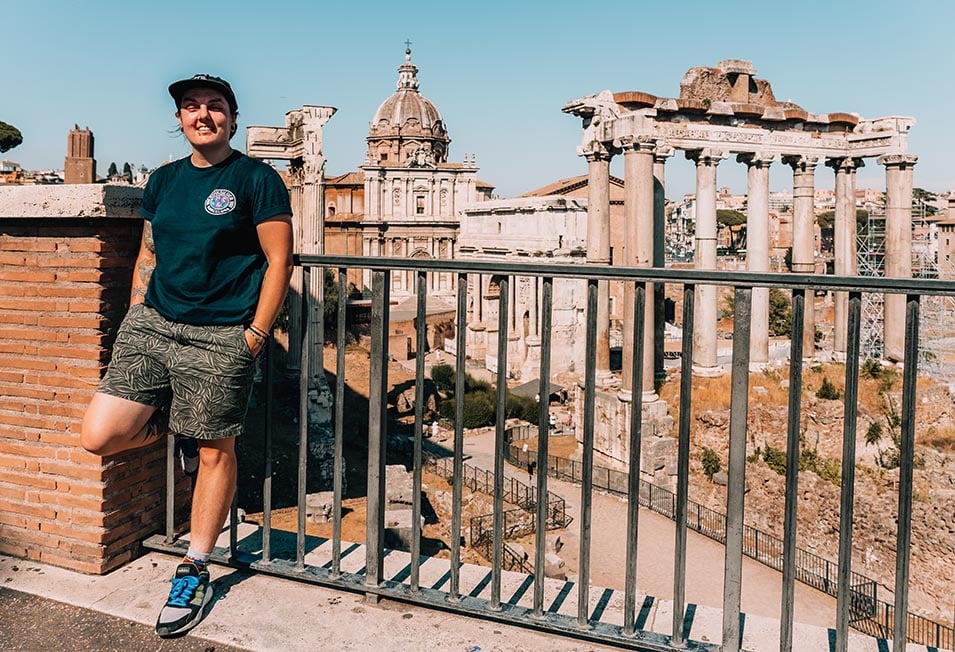 A person standing leaning against some railings with The ruins of the Roman Forum behind in Rome, Italy