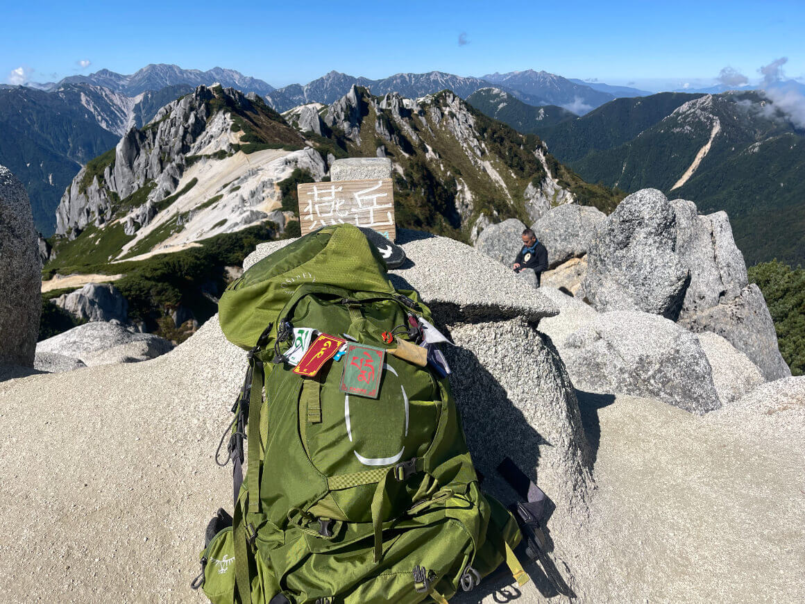 green Aether Backpack sitting on a rock with lush green mountains off in the distance in japan