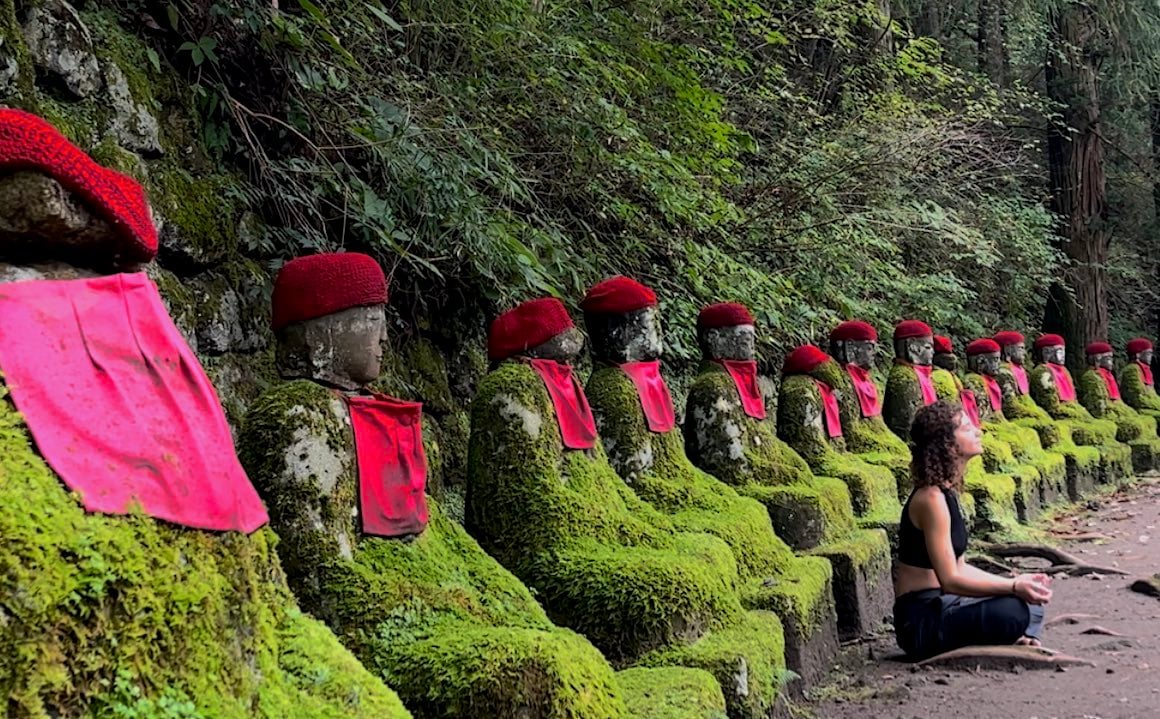 A girl meditates amongst buddha statues at temple in Nikko, Japan.