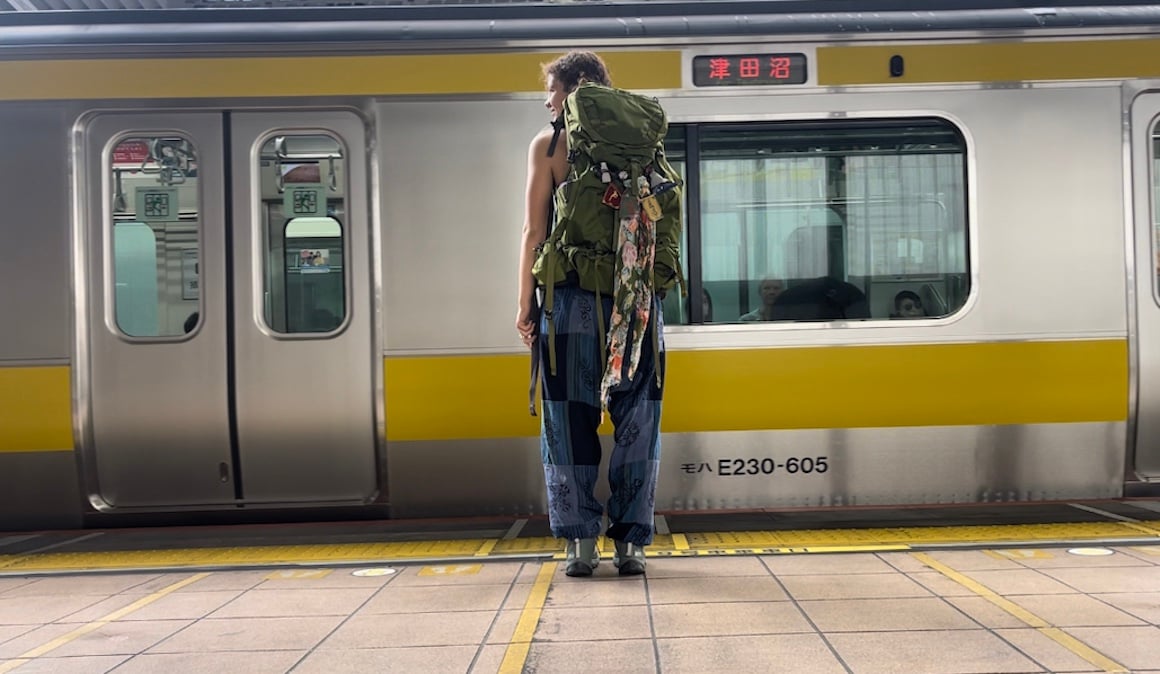 Girl stands in front of train in Tokyo, Japan with her backpack on.