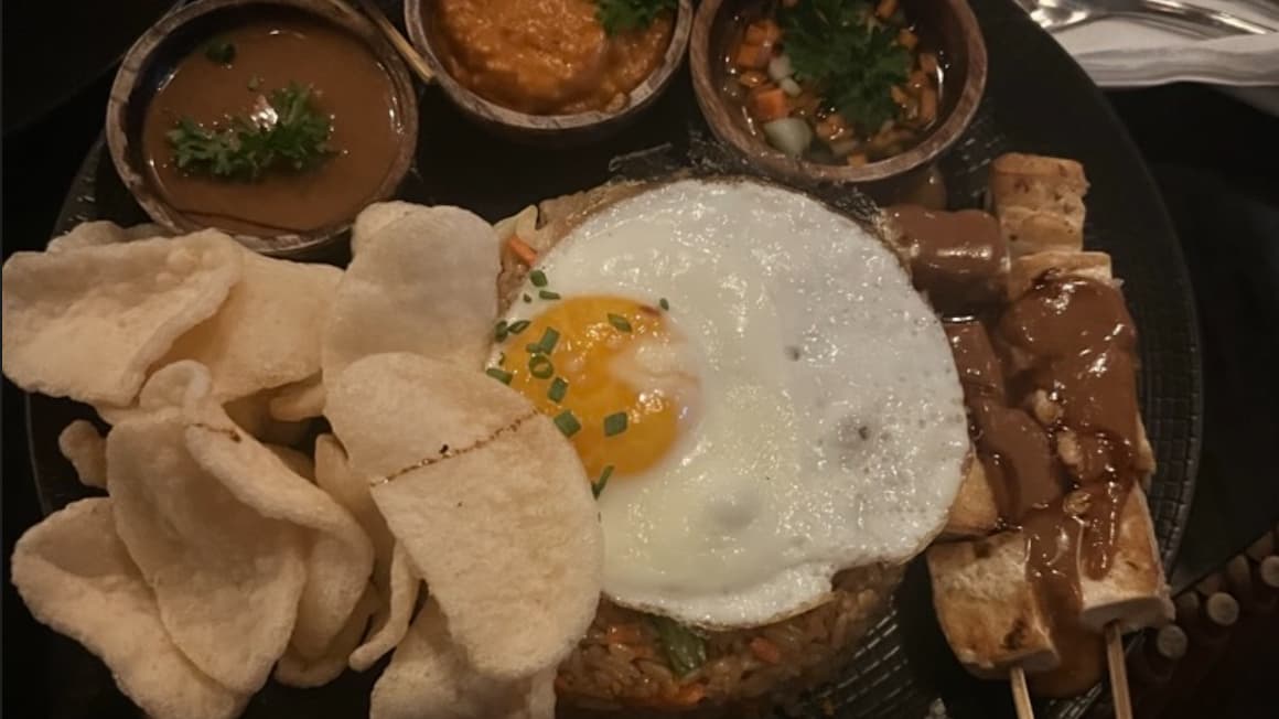 a traditional plate of indonesian food called nasi goreng, with fried rice, a fried egg, chicken, and peanut sauce