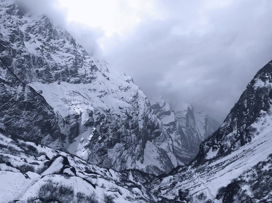 massive snow covered mountains in nepal among a dark cloudy grey sky as a snow storm rolls in during a hike