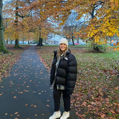 Girl in a big coat walking through the park surrounded by autumn leaves.