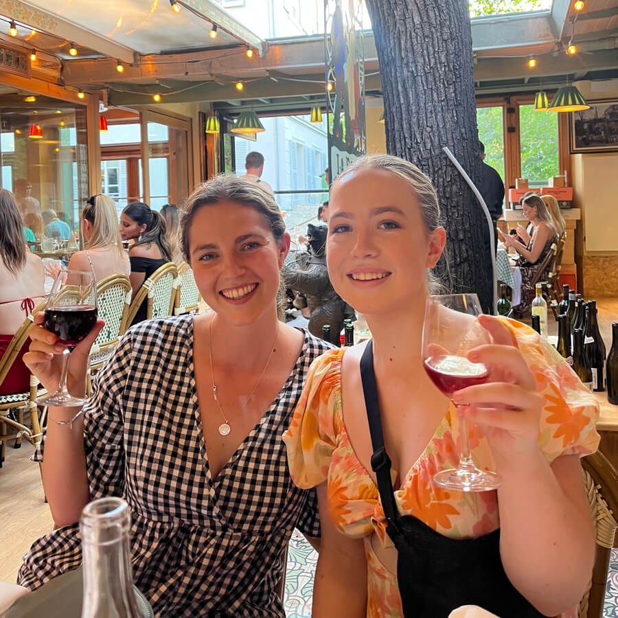 Two girls sitting at a restaurant table smiling holding wine
