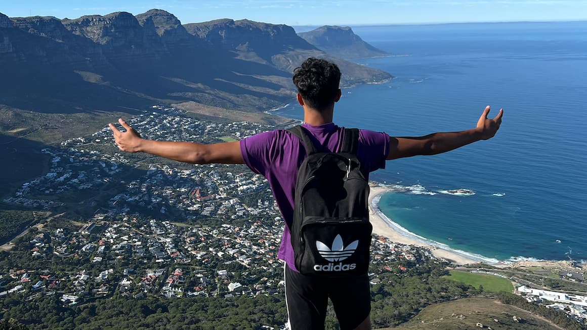 a guy hiking in Cape Town, with a view of the ocean and mountains