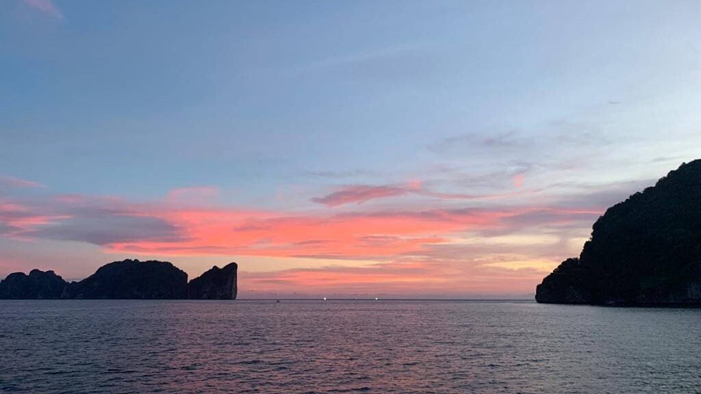 A landscape view of a sunset over the ocean with colorful skies and islands in the distance.