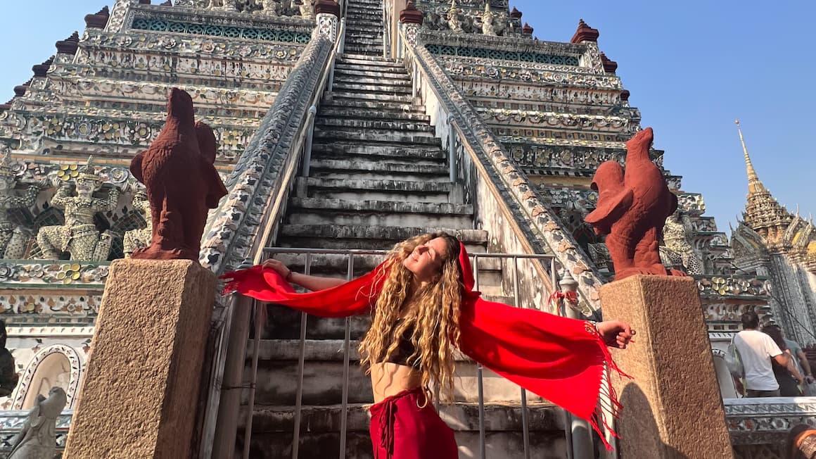 a girl in front of wat arun, temple in thailand feeling happy 