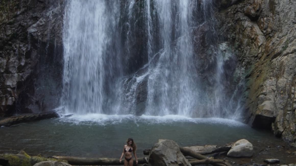 a girl under a tall waterfall in thailand 