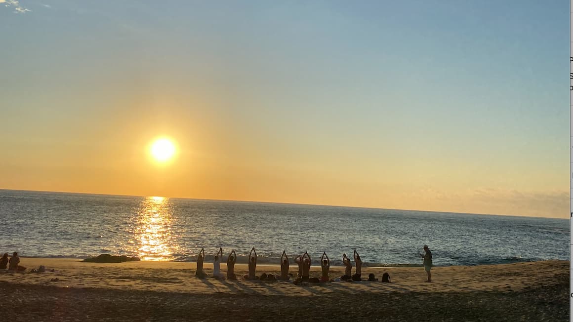 a group of people doing yoga in a sitting position by the beach as the sunsets 