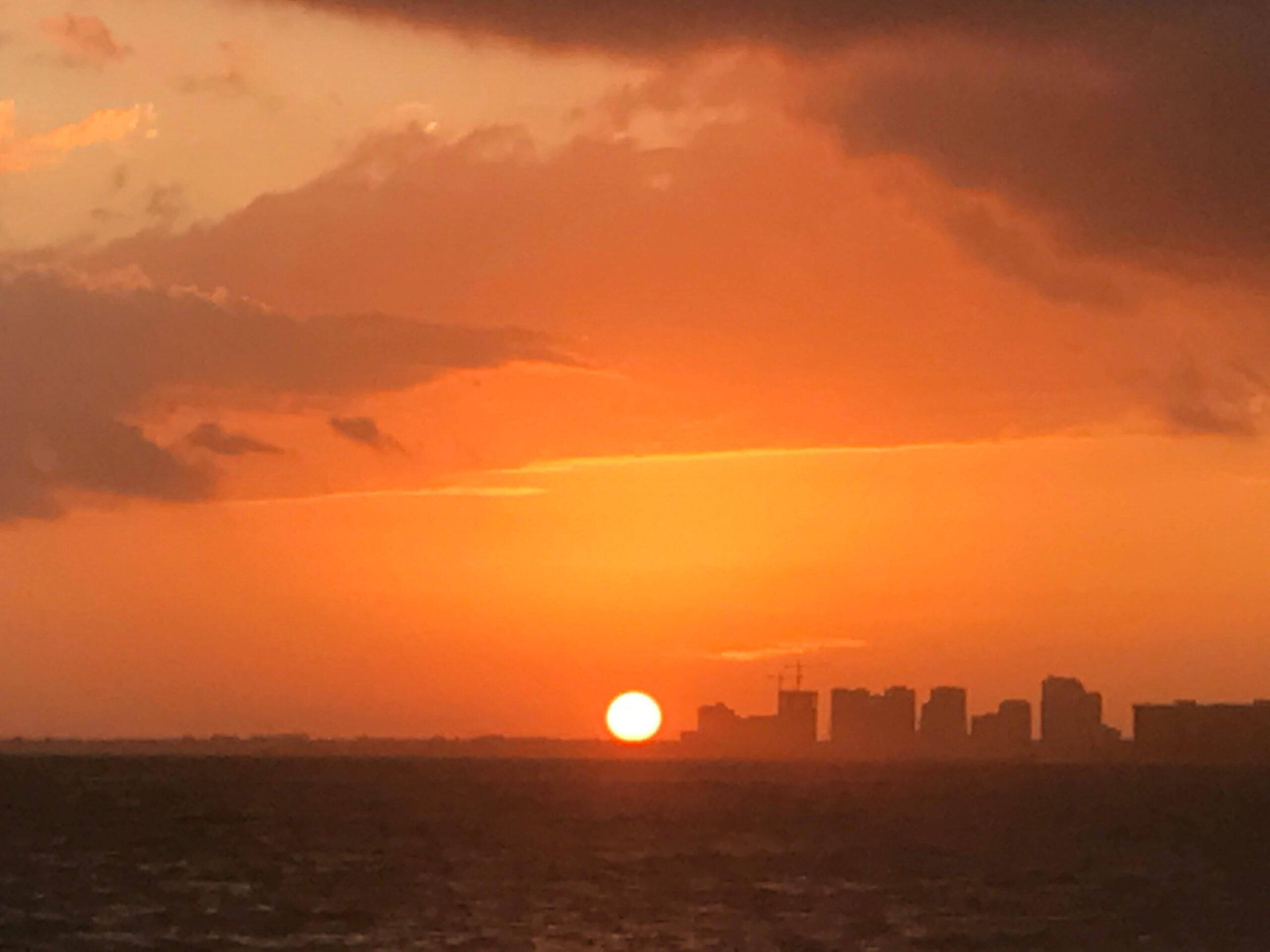 a bright orange sunset over a beach with some high rise buildings in the background seen while staying in miami florida
