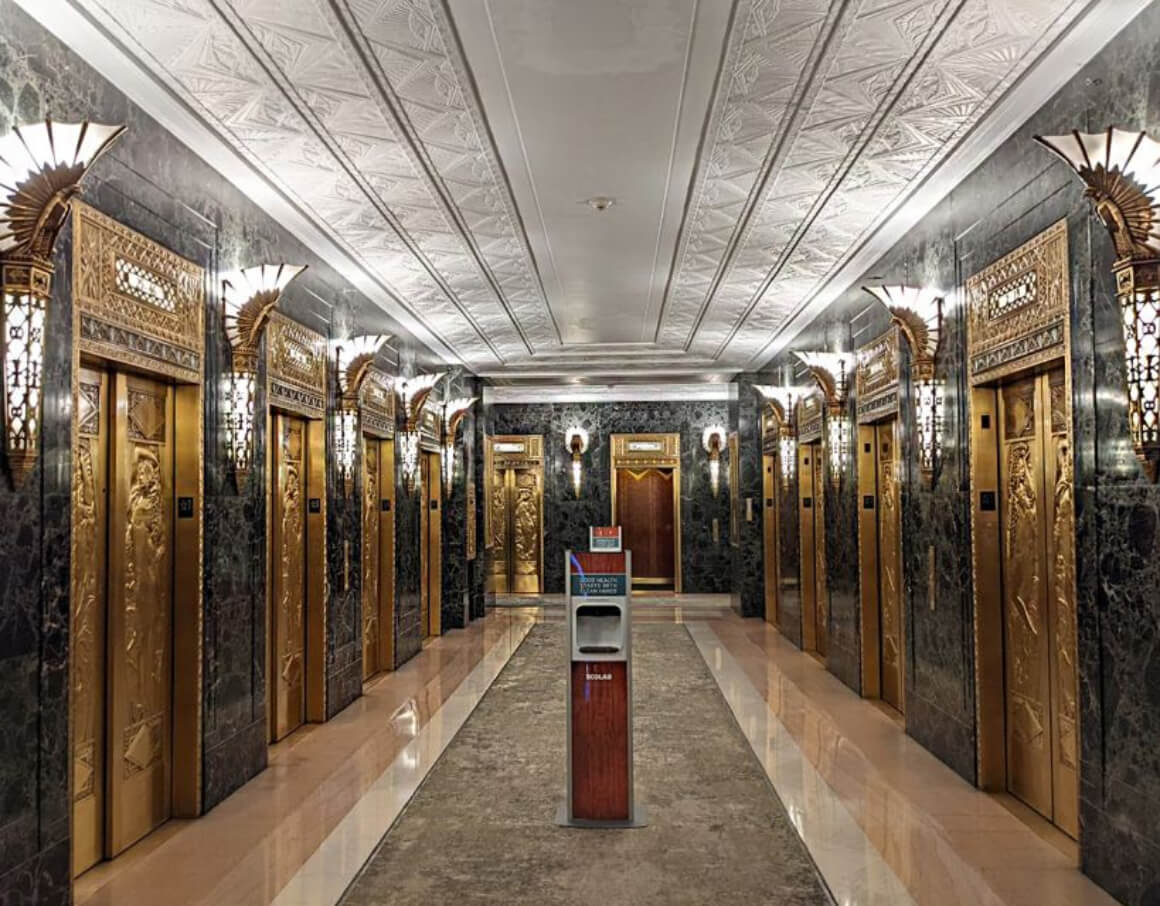 A long hallway with a polished marble floor and chrome-plated elevator doors.