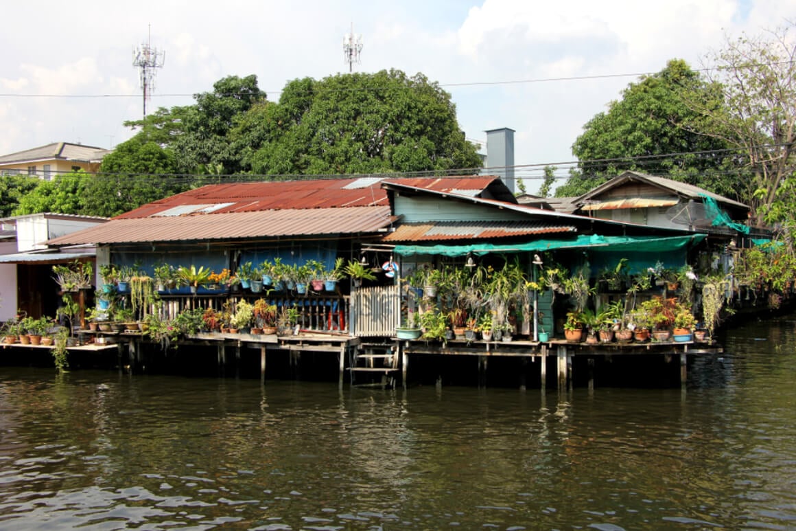 Artist’s House on stilts perched above a river in Bangkok, Thailand, with colorful plants overflowing from its balcony.