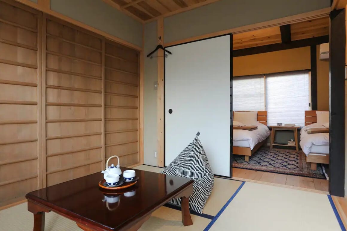 A room with a table set for tea in an Authentic Restored Kyo Machiya House with a sliding door in the background leading to a bedroom.