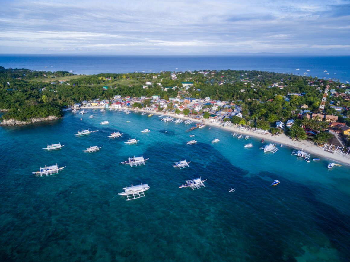 a lanscape view of Malapascua island with lush greenery and boats floating on a the bay.